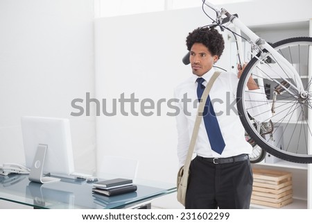 Attractive businessman carrying his bike in his office