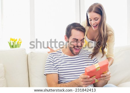 Pretty woman surprising her boyfriend with gift at home in the living room