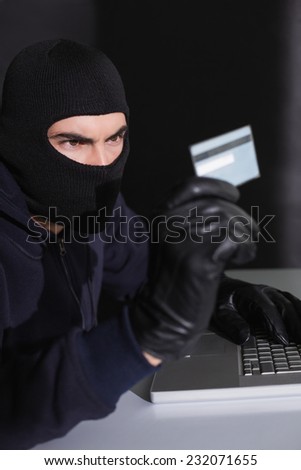 Hacker in balaclava spending money online on black background