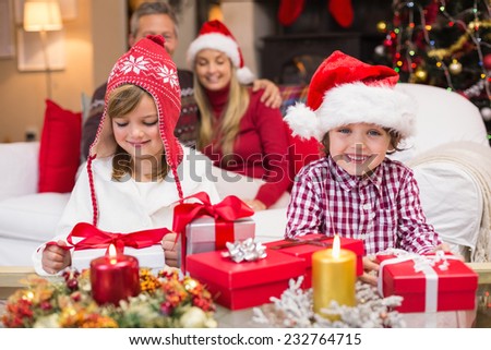 Festive little siblings opening a gift in front of their parents at home in the living room