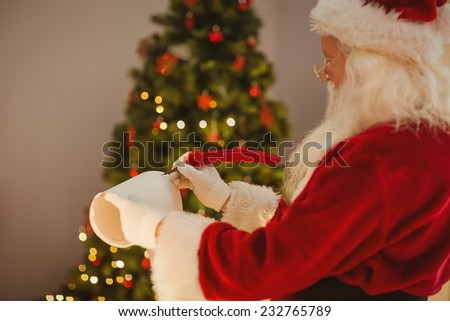 Santa claus writing with a quill at home near the christmas tree