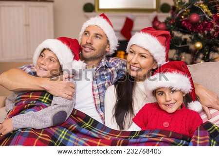 Happy family in santa hat hugging under the cover at home in the living room