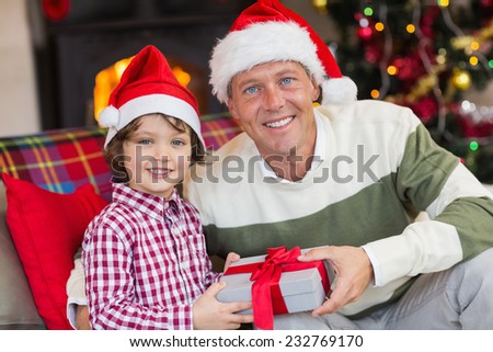 Son offering father a christmas gift on the couch at home in the living room