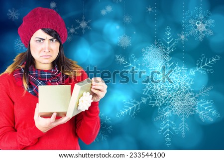 Unhappy brunette opening christmas gift against blue snow flake pattern design