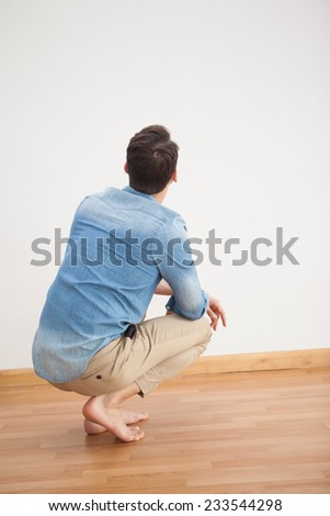 Casual man crouching on floor looking at wall at home in the living room