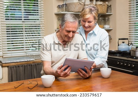 Senior couple looking at tablet pc together at home in the kitchen