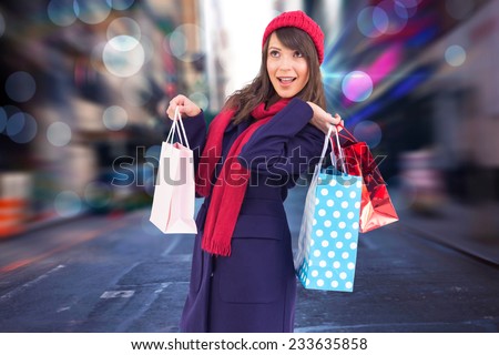 Young woman in winter clothes posing with shopping bags against blurry new york street