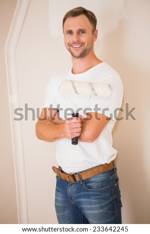 Smiling handyman posing while holding a paintbrush in a new house