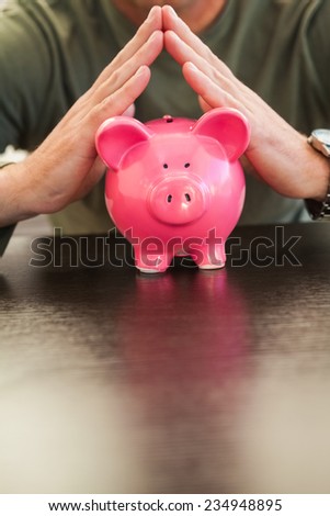 Mid section of a man with joined hands on piggy bank at home in the living room