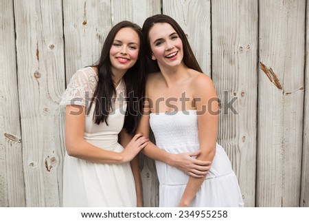 Pretty friends smiling in white dresses against bleached wooden planks