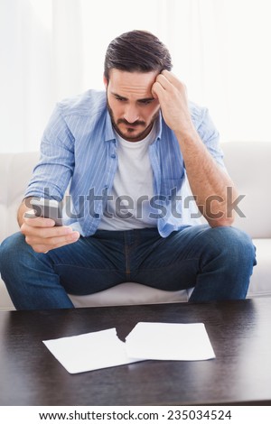 Worried man holding his phone in the living room