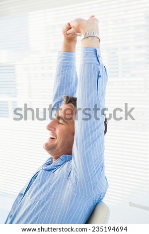 Happy businessman stretching his arms in his office
