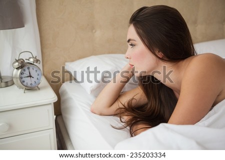 Pretty brunette looking at her alarm clock at home in the bedroom