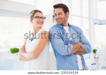 Editors posing with arms crossed looking at each other in office