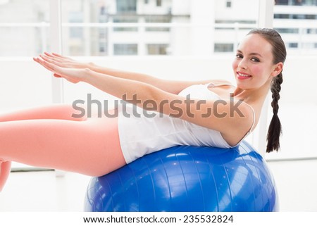 Fit brunette stretching on an exercise ball by a large window at home