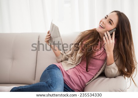 Pretty brunette on the phone holding newspaper at home in the living room