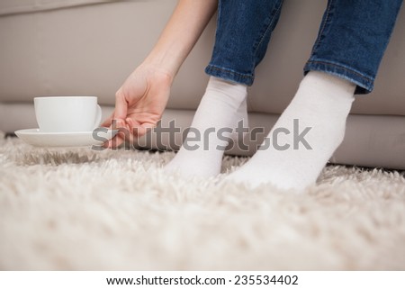 Woman picking up cup and saucer at home in the living room