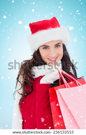 Cheerful brunette in winter wear holding shopping bags against blue background with vignette