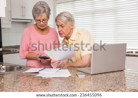 Senior couple paying their bills with laptop at home in the kitchen