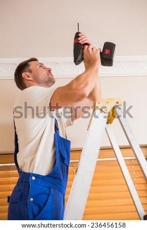 Handyman using a cordless drill to the ceiling in a new house