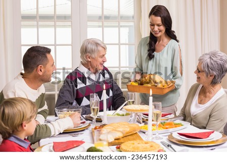 Woman holding turkey roast with family at dining table at home in the living room