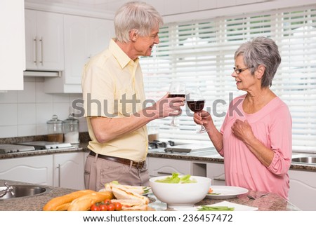Senior couple preparing lunch together having red wine at home in the kitchen
