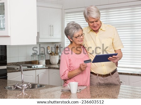 Senior couple shopping online with tablet pc at home in the kitchen