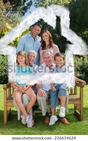 Smiling multi generation family sitting on bench in park against house outline in clouds