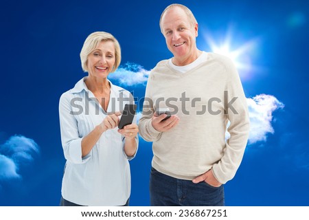 Happy mature couple using their smartphones against bright blue sky with clouds
