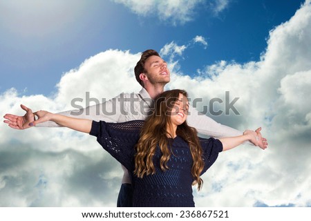 Romantic young couple with arms out against blue sky with clouds