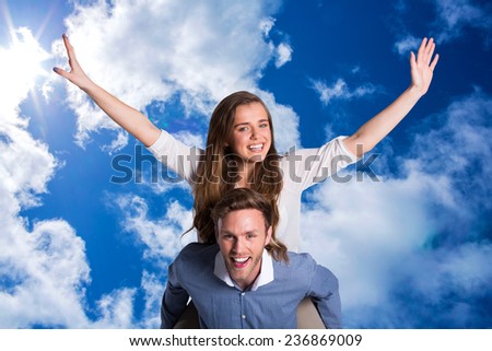 Smiling young man carrying woman against bright blue sky with clouds