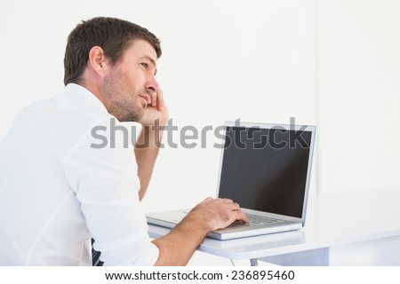Thinking businessman sitting at desk using laptop on white background