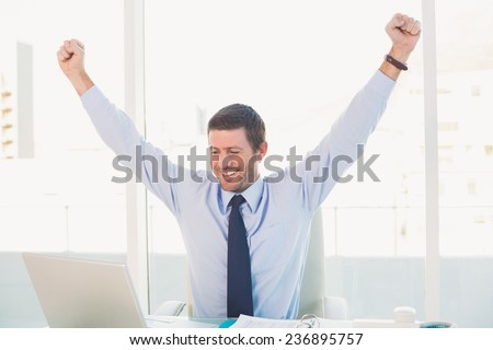 Cheering businessman at his desk in his office