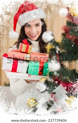 Festive brunette holding pile of gifts near a christmas tree against christmas theme frame in silver