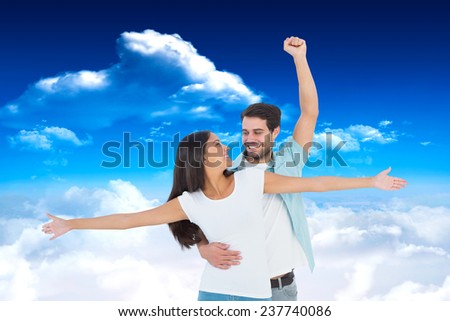 Happy casual couple cheering together against bright blue sky with clouds