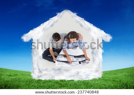 Overview of a husband and his wife looking at house plans against green field under blue sky