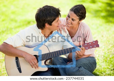 Man and his friend look at each other while he is playing the guitar against house outline