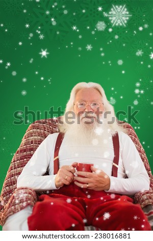 Father christmas sitting on the armchair holding mug against red background