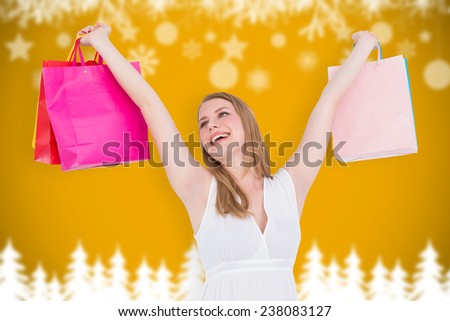 Blonde woman raising shopping bags against blurred fir tree background