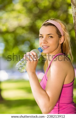 Fit blonde leaning against tree drinking water on a sunny day