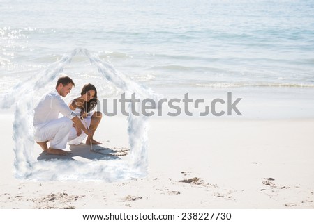 Cute couple drawing a heart in the sand against house outline in clouds