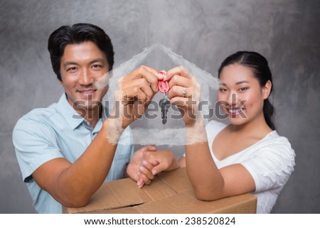 Happy couple holding house key and leaning on moving box against house outline in clouds