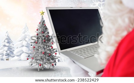 Father christmas using his laptop against christmas tree in snowy landscape