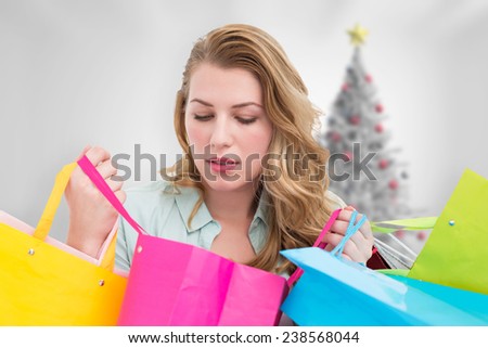 Blonde woman opening gift bag and looking on it against blurry christmas tree in room
