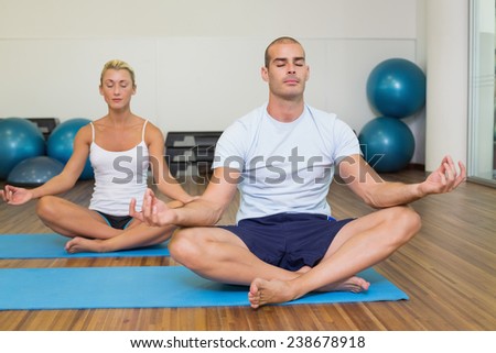 Sporty young couple sitting in lotus posture with eyes closed at fitness studio