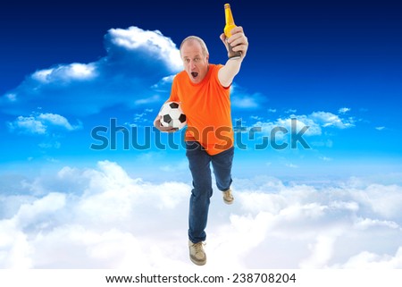 Mature man in orange tshirt holding football and beer against bright blue sky with clouds