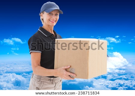 Happy delivery woman holding cardboard box against mountain peak through clouds