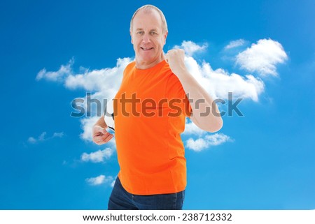 Mature man in orange tshirt cheering holding football against cloudy sky