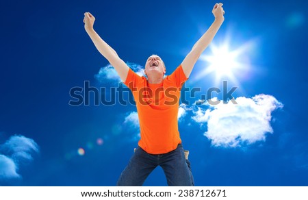 Mature man in orange tshirt cheering while kneeling against bright blue sky with clouds