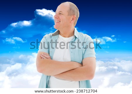 Happy older man with arms crossed against bright blue sky with clouds
